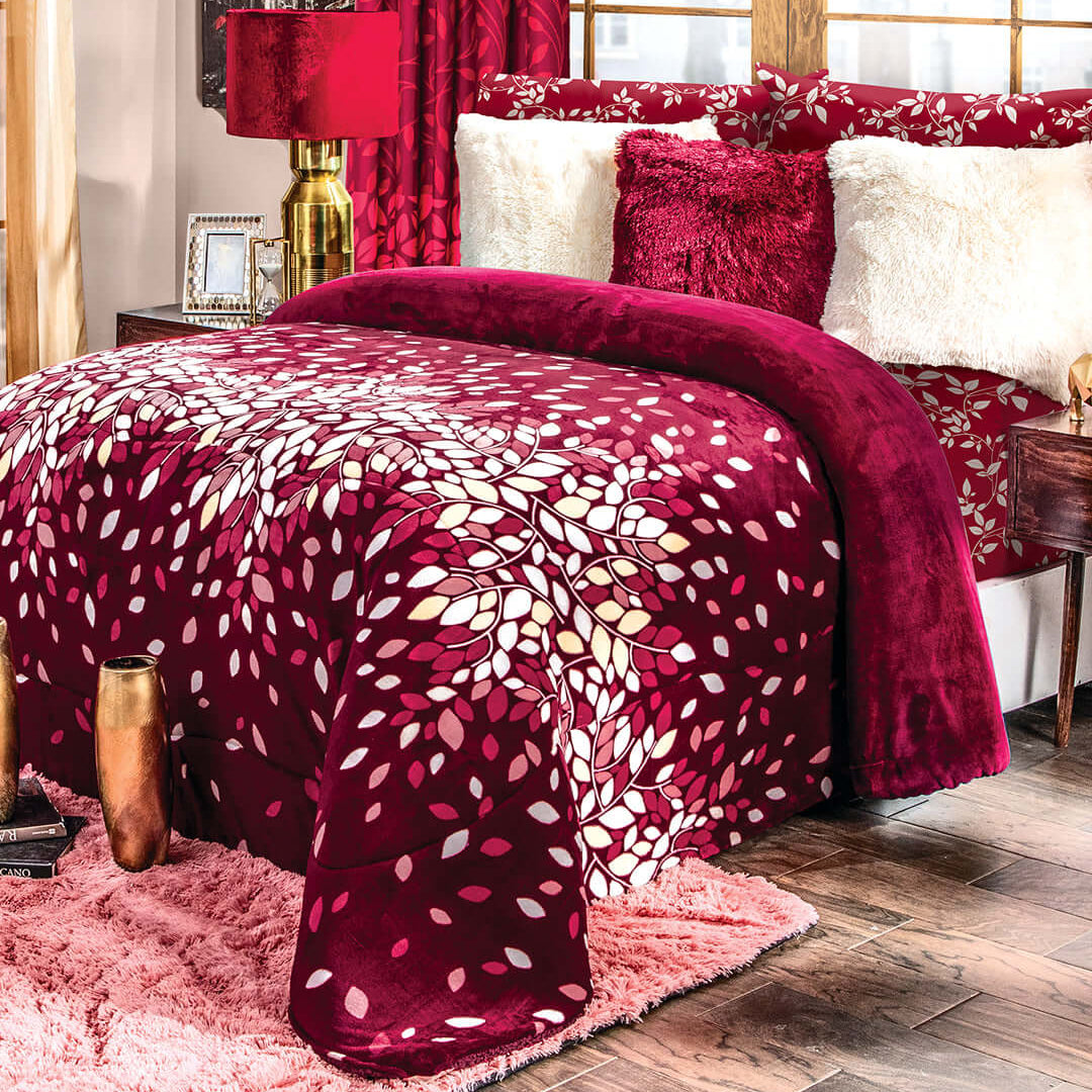 A cozy bedroom with a red and white leaf-patterned comforter, red and white pillows, a pink shag rug, wood flooring, and gold and red decor near large windows with snowy trees outside.
