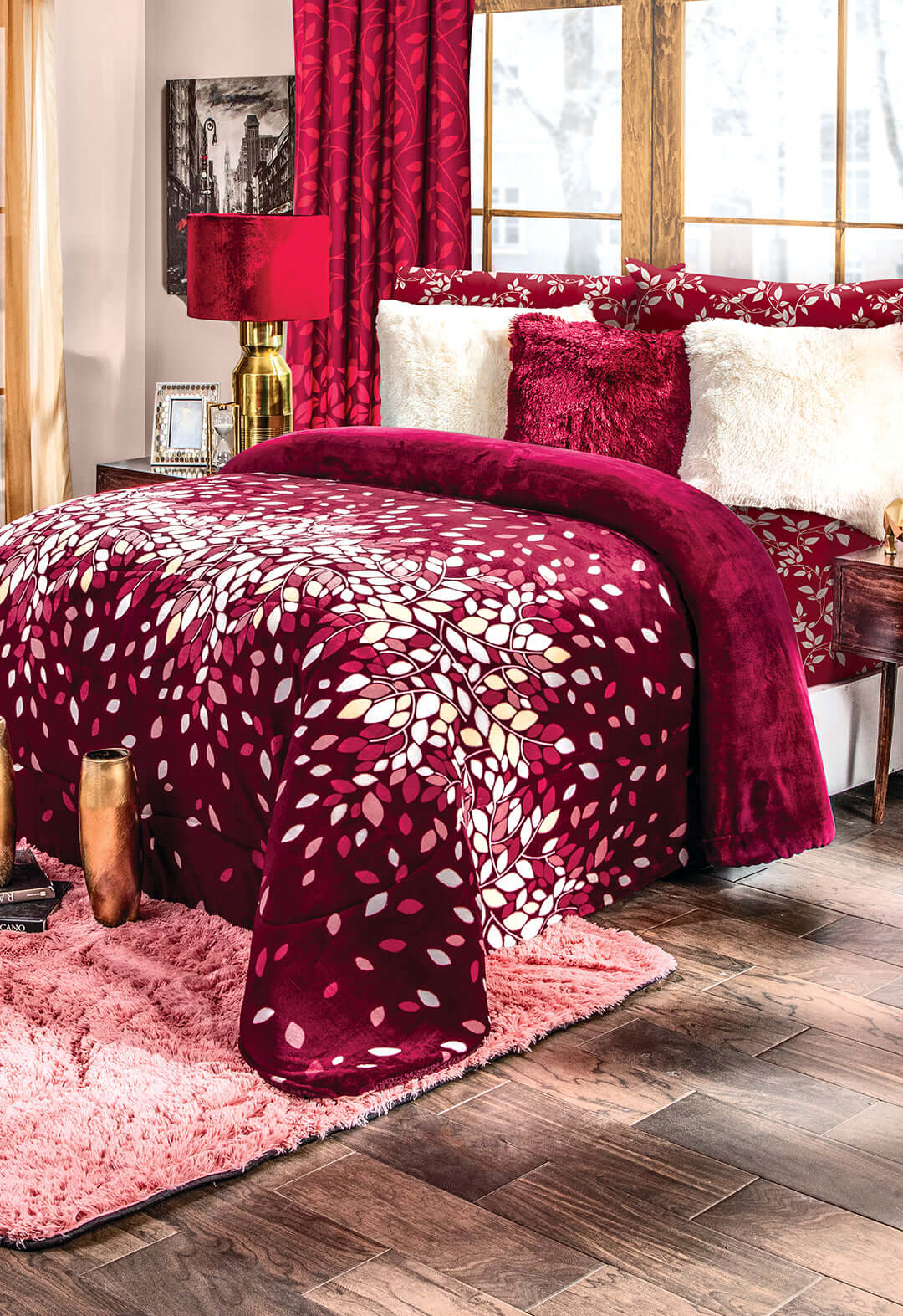 A cozy bedroom with a red and white leaf-patterned comforter, red and white pillows, a pink shag rug, wood flooring, and gold and red decor near large windows with snowy trees outside.