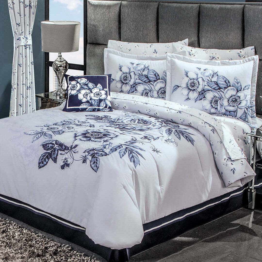 A modern bedroom with a gray headboard, light blue quilt, multiple pillows, a wooden nightstand with a lamp and flowers, and a black shelf with decor items against a gray wall and tiled floor.