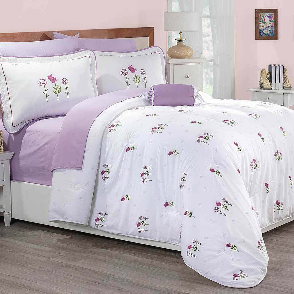 A neatly made bed with white and lavender bedding, adorned with embroidered pink and purple flowers, in a cozy bedroom with light pink walls and decorative accents.