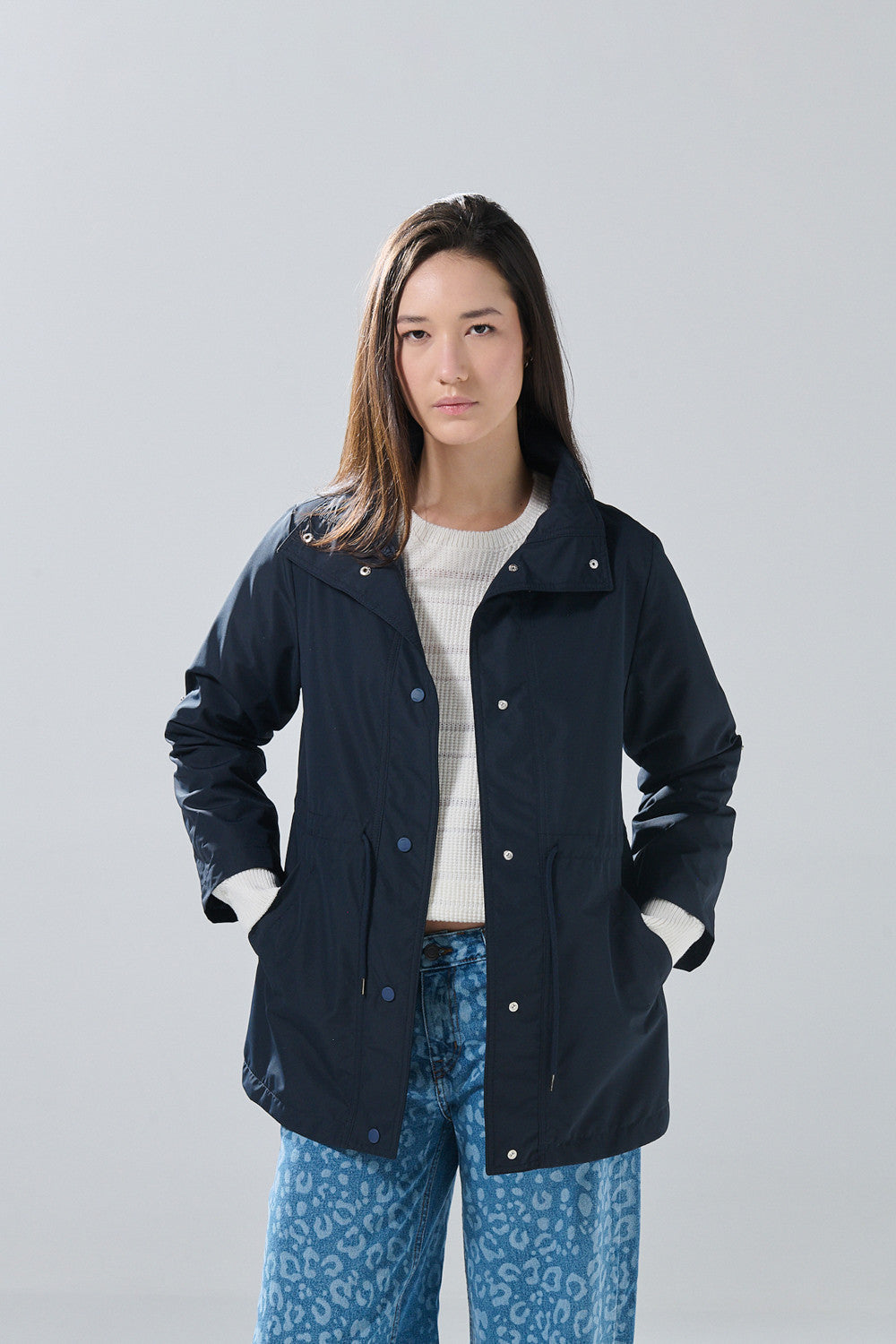 A woman stands facing forward against a plain light gray background, wearing the KOAJ CHAQUETA KOAJ CHARAMONYD 1 4/25 in navy by KOAJ over a white sweater and blue leopard-print jeans.