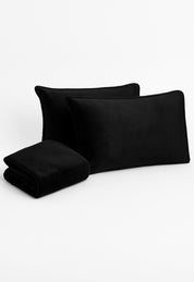 Two black rectangular pillows and a matching folded franela suave blanket from the Juego de Sábanas Invernales Negro by Intima Hogar are arranged on a white background.