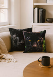 Dos cojines Cojín Estampado Black Panther de Intima Hogar descansan sobre un sofá beige junto a una manta, mientras libros y decoración llenan las estanterías y una taza de café reposa en la mesa enfrente.