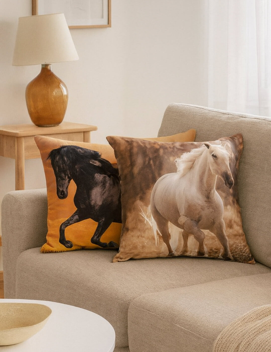 Two Cojín Estampado Caballo pillows by Intima Hogar, featuring realistic horse prints, are displayed on a light beige sofa in a cozy living room with soft natural light and elegante decoración.
