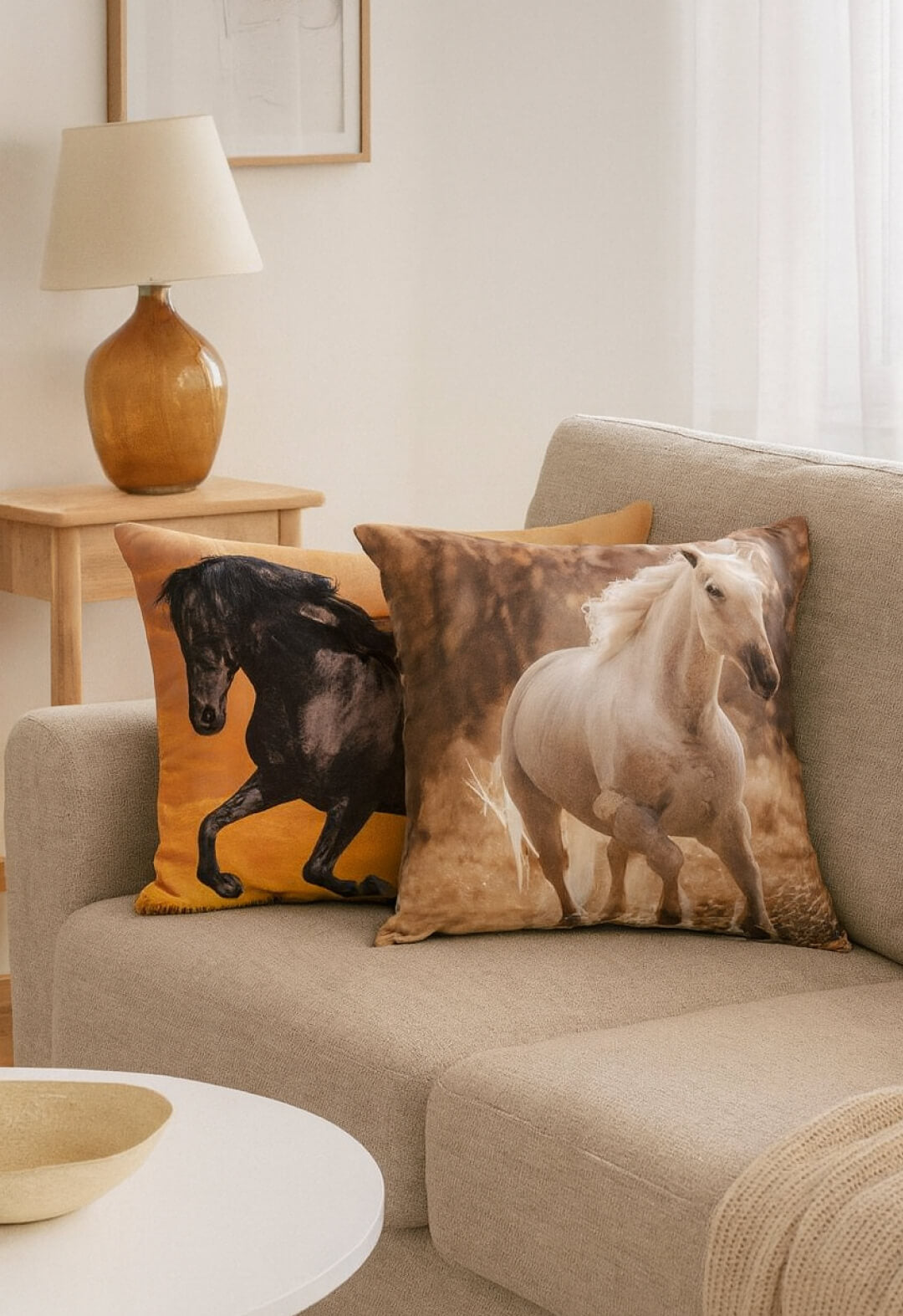 Two Cojín Estampado Caballo pillows by Intima Hogar, featuring realistic horse prints, are displayed on a light beige sofa in a cozy living room with soft natural light and elegante decoración.