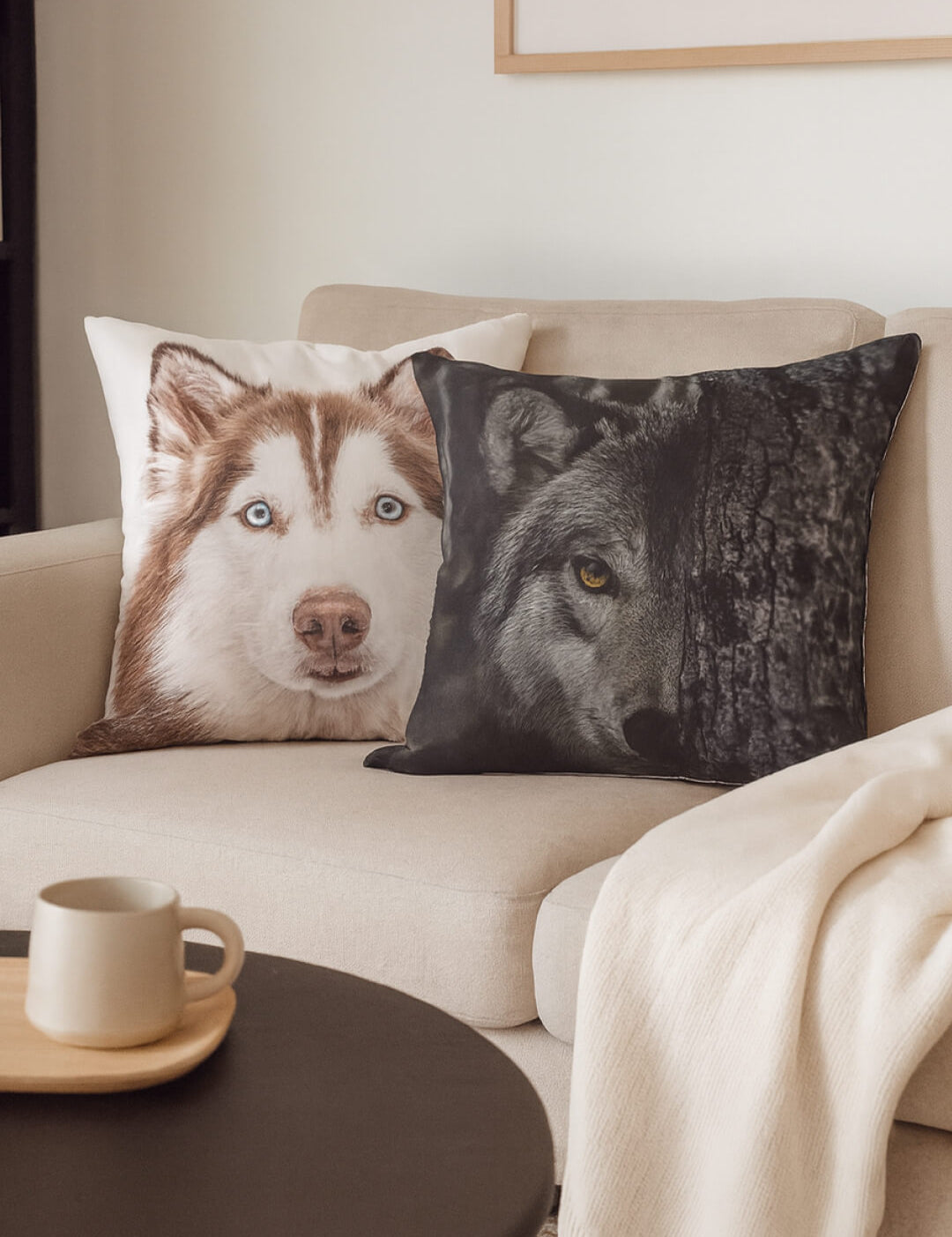 On a beige couch, two cojines decorativos—including Intima Hogar’s Cojín Estampado Lobo—add visual flair. A cream throw and a round coffee table with a cup complete the cozy setting.