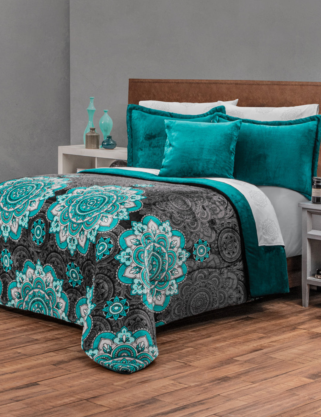 A bed with a teal and gray mandala-patterned comforter, teal pillows, and wooden headboard sits in a modern bedroom. The Coordinado de Cobertor Supremo Tíbet by Intima Hogar adds calidez duradera, with a nightstand beside the bed.