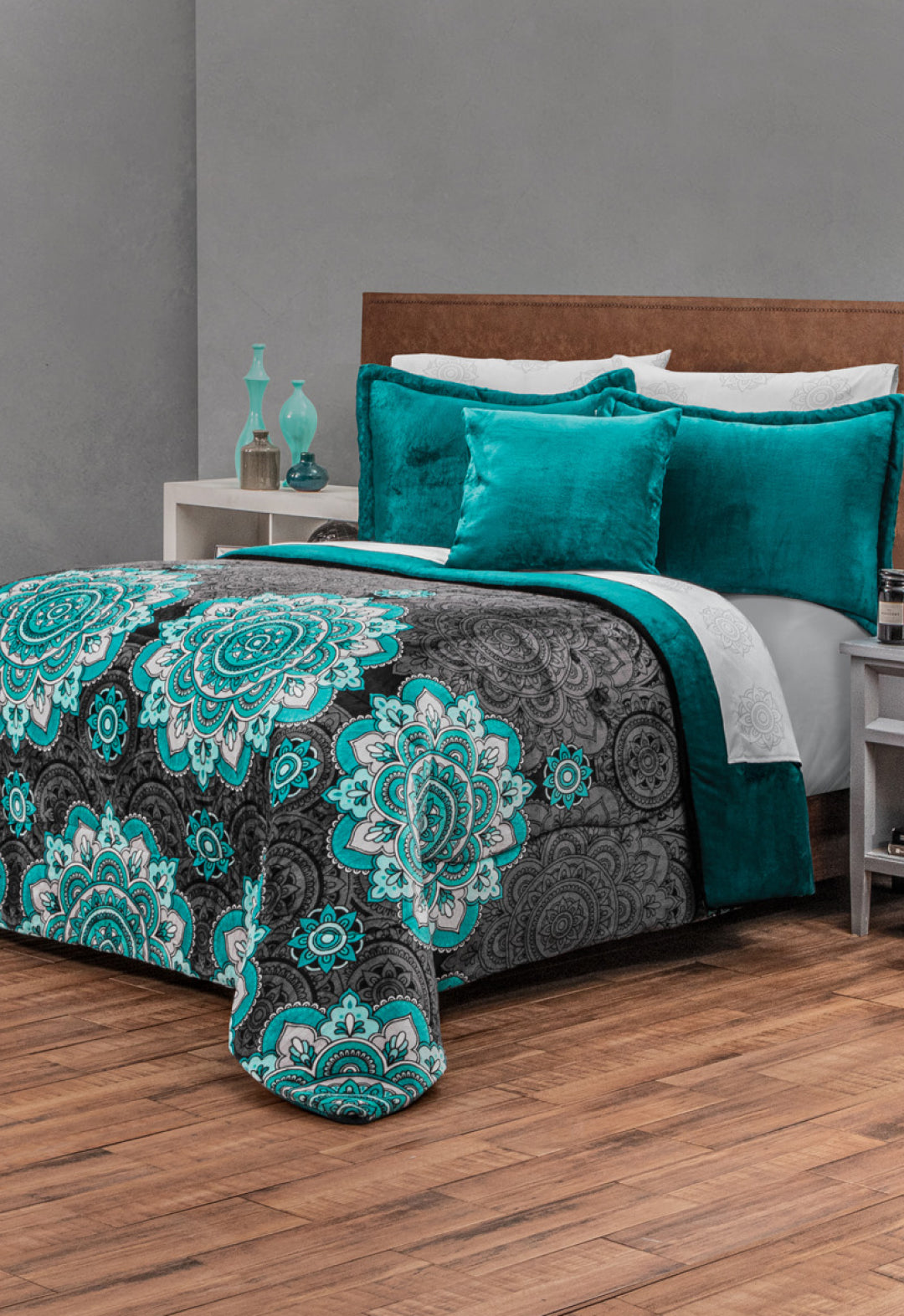 A bed with a teal and gray mandala-patterned comforter, teal pillows, and wooden headboard sits in a modern bedroom. The Coordinado de Cobertor Supremo Tíbet by Intima Hogar adds calidez duradera, with a nightstand beside the bed.