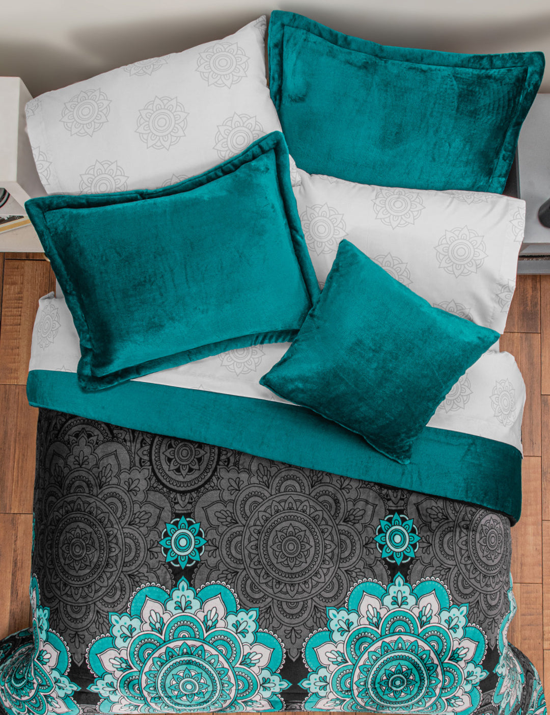 The Coordinado de Cobertor Supremo Tíbet de Intima Hogar, con cojines y manta en terciopelo teal, sábanas blancas con mandalas y cobertor franela negro y teal, luce acogedor sobre piso de madera.