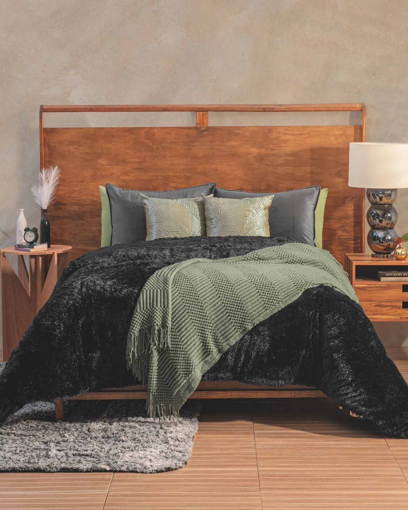 A neatly made bed with a wooden headboard features an Intima Hogar Cobertor Platinum Extra Suave Albania, green throw, and matching pillows for an ambiente elegante. Wooden nightstands hold lamps and decor. A gray rug accents the floor.
