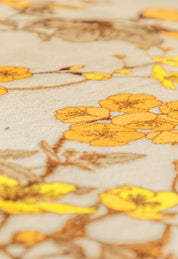 Close-up of the Cobertor Flannel Extra Suave Colombia by Intima Hogar, featuring a soft beige floral design with yellow and orange flowers and brown stems, creating a gently blurred, cozy look for your cama.