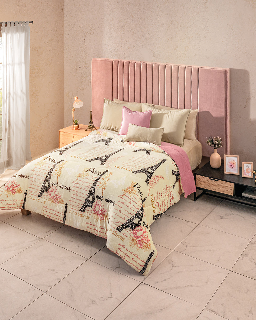 A bright bedroom features a neatly made bed with Eiffel Tower print bedding, pink pillows, the Intima Hogar Cobertor Flannel Extra Suave Francia-Desc, a pink velvet headboard, bedside tables, lamps, and framed pictures.