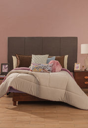 A neatly made bed with pillows, one reading "Tropical," features the Intima Hogar Cobertor Flannel Extra Suave Italia against a pink wall and dark headboard. Two wooden nightstands with lamps, photos, and a vase add cozy modern style.