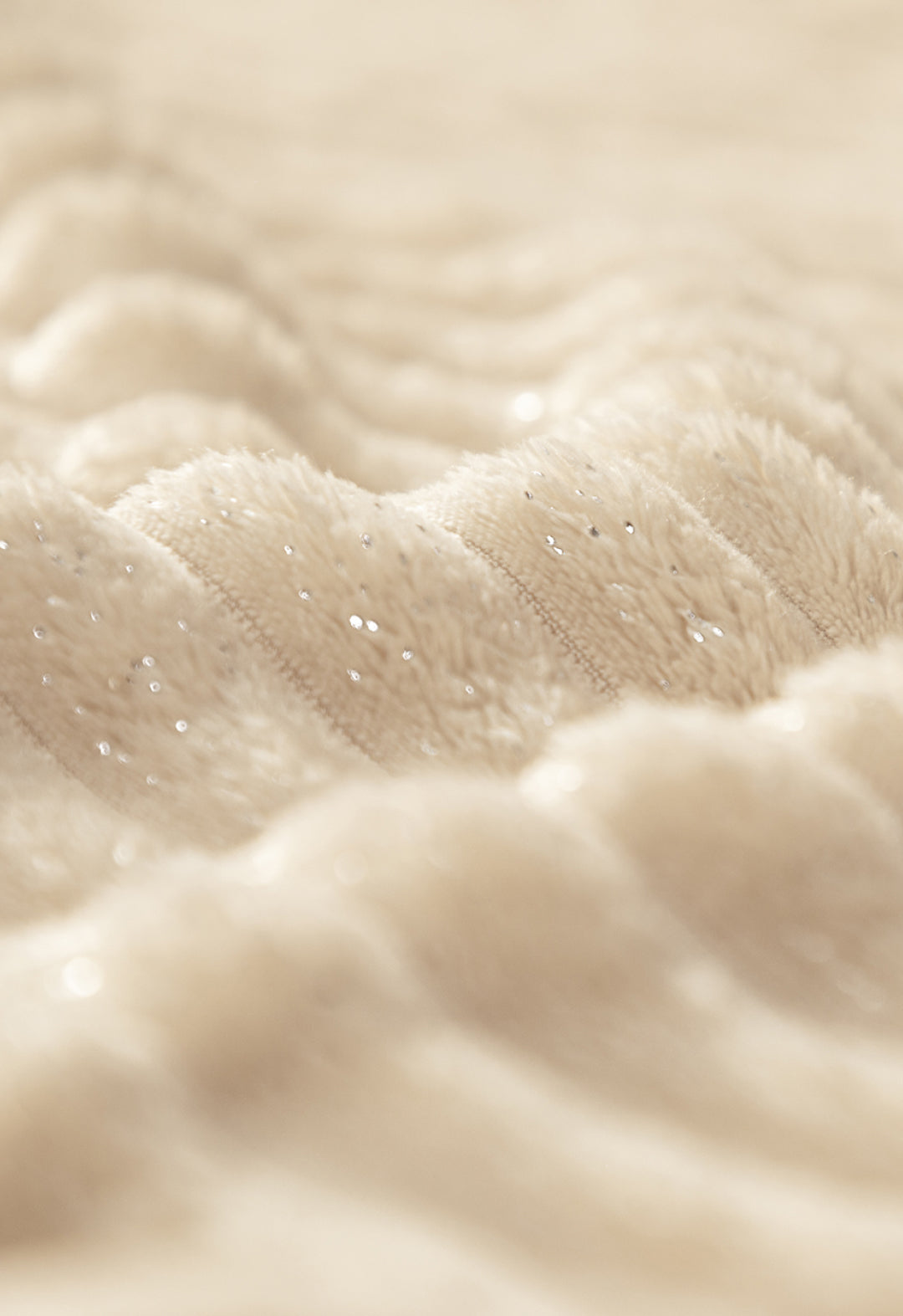 Close-up of the Cobertor Flannel Ligero Jasper by Intima Hogar: a soft, cream-colored blanket with subtle stitched lines and sparkling specks. Resistant to washing, it offers a cozy, plush, and inviting feel.