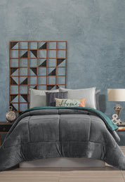 A neatly made bed with gray and teal bedding features the Intima Hogar Cobertor Flannel Extra Suave Mediterráneo for a cozy touch, accented by patterned and Home pillows. A wooden geometric wall piece decorates the textured blue wall behind the bed.