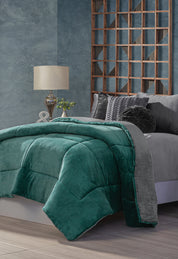 A modern bedroom with a gray bed featuring the Cobertor Flannel Extra Suave Mediterráneo by Intima Hogar, dark teal and gray bedding, decorative pillows, a silver lamp, a small plant on the side table, and a textured blue-gray wall with wooden lattice accents.