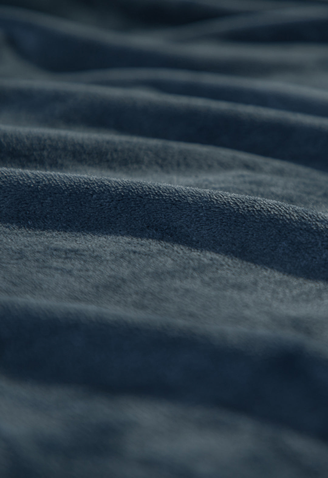 Close-up of the Cobertor Flannel Ligero Ontario Azul Marino by Intima Hogar, featuring gentle, wavy folds and a textured, soft surface highlighted by the lighting for added depth and smoothness.