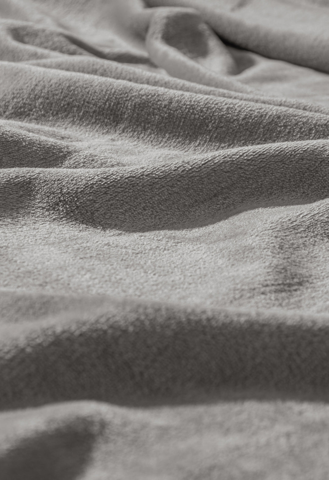 Close-up of the Cobertor Flannel Ligero Ontario Gris by Intima Hogar, featuring soft, textured gray fabric with gentle folds and light shadows for a cozy and comfortable look.