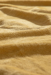 Close-up of the Cobertor Flannel Ligero Ontario Oro by Intima Hogar, showing its textured yellow flannel surface with soft folds and gentle shadows that create a wavy pattern.