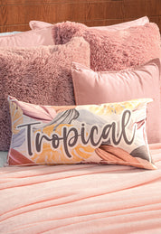 A bed features the Intima Hogar Cobertor Flannel Ligero Ontario Rosa, paired with soft, textured pink pillows and a rectangular accent pillow decorated with pastel leaves and "Tropical" boldly scripted.