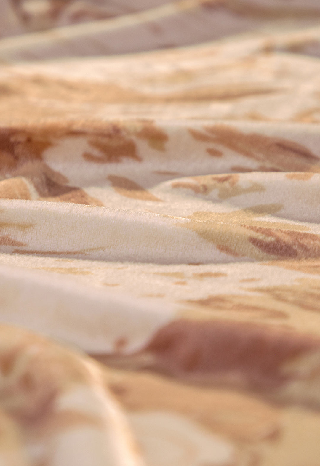 Soft focus close-up of the Cobertor Flannel Ligero Tajín by Intima Hogar in beige and light brown tones, showing gentle folds and wavy texture with a subtle interplay of light and shadow across its soft surface.