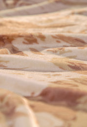 Soft focus close-up of the Cobertor Flannel Ligero Tajín by Intima Hogar in beige and light brown tones, showing gentle folds and wavy texture with a subtle interplay of light and shadow across its soft surface.