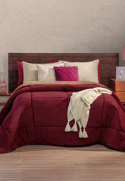 A neatly made bed with a dark wooden headboard, burgundy comforter, beige and burgundy pillows, and a cream knit throw—perfect for invierno with the Cobertor Flannel Extra Suave Viñedo by Intima Hogar for cozy warmth.