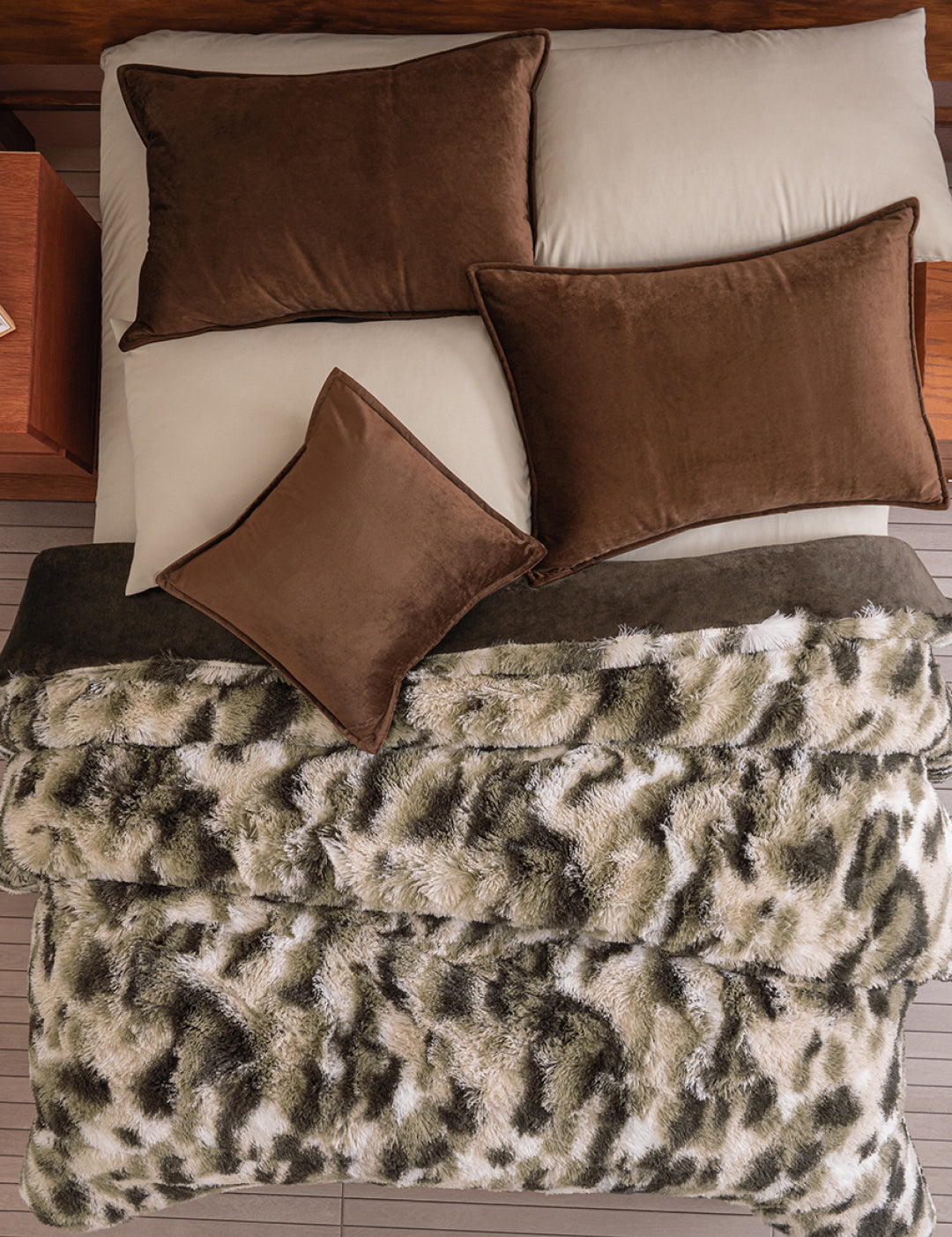Overhead view of a neatly made bed with tan sheets, brown pillows, and the Cobertor Platinum Extra Suave Finlandia by Intima Hogar—a plush franela faux fur blanket in a gray, black, and white animal print pattern.