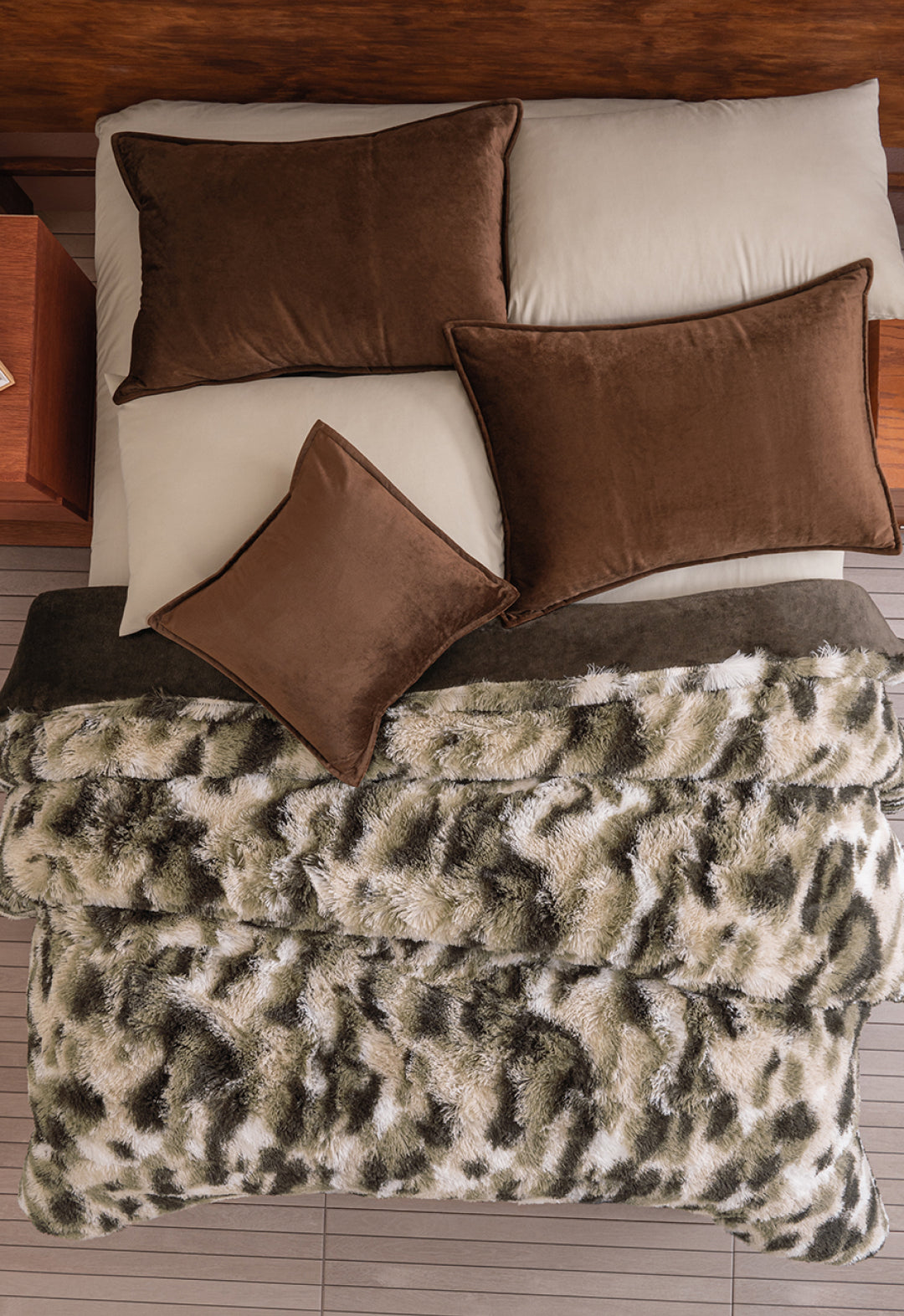 Overhead view of a neatly made bed with tan sheets, brown pillows, and the Cobertor Platinum Extra Suave Finlandia by Intima Hogar—a plush franela faux fur blanket in a gray, black, and white animal print pattern.