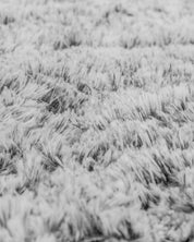 Close-up of the Frazada de Lujo Humo by Intima Hogar, featuring soft, fluffy gray fabric with detailed fibers and a wavy pattern, evoking frescura y comodidad and adding coziness and warmth to any space.