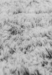 Close-up of the Cobertor Platinum Extra Suave Humo by Intima Hogar, showing its ultra-soft, fluffy gray and white texture with visible fibers and a gentle wavy pattern, resembling luxurious furry fabric.