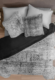 A neatly made bed with two gray pillows, two gray shaggy throw pillows, a black blanket, and a soft Cobertor Platinum Extra Suave Humo by Intima Hogar, all set on a wooden floor.