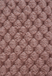 Close-up of the Cobertor Platinum Extra Suave Aruba by Intima Hogar: a plush, ultra-soft texture with raised, fluffy bumps in muted pink—perfect for a cozy winter blanket and an inviting, comfy touch.