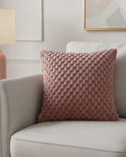 El Cojín de Lujo Aruba de Intima Hogar, en tono malva y con textura de puntos en relieve, decora un sillón gris claro en una sala moderna con luz suave.