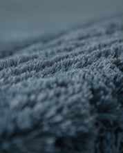 Close-up of soft, plush blue-grey fabric with a thick, fuzzy texture—ideal for Cojines de Lujo Bruselas by Intima Hogar. The densely woven fibers create a cozy, luxurious look for any space.