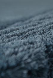 Close-up of the soft, blue-gray Frazada de Lujo Bruselas by Intima Hogar, showing plush textured fibers in sharp detail against a softly blurred background for a luxurious, cozy look.