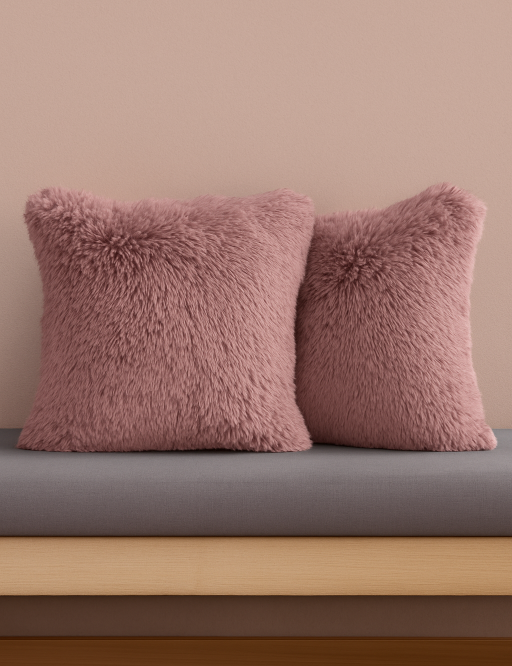 Two pink, fluffy Cojines de Lujo Liverpool by Intima Hogar are placed side by side on a gray cushion against a light pink wall, resting on a wooden bench.