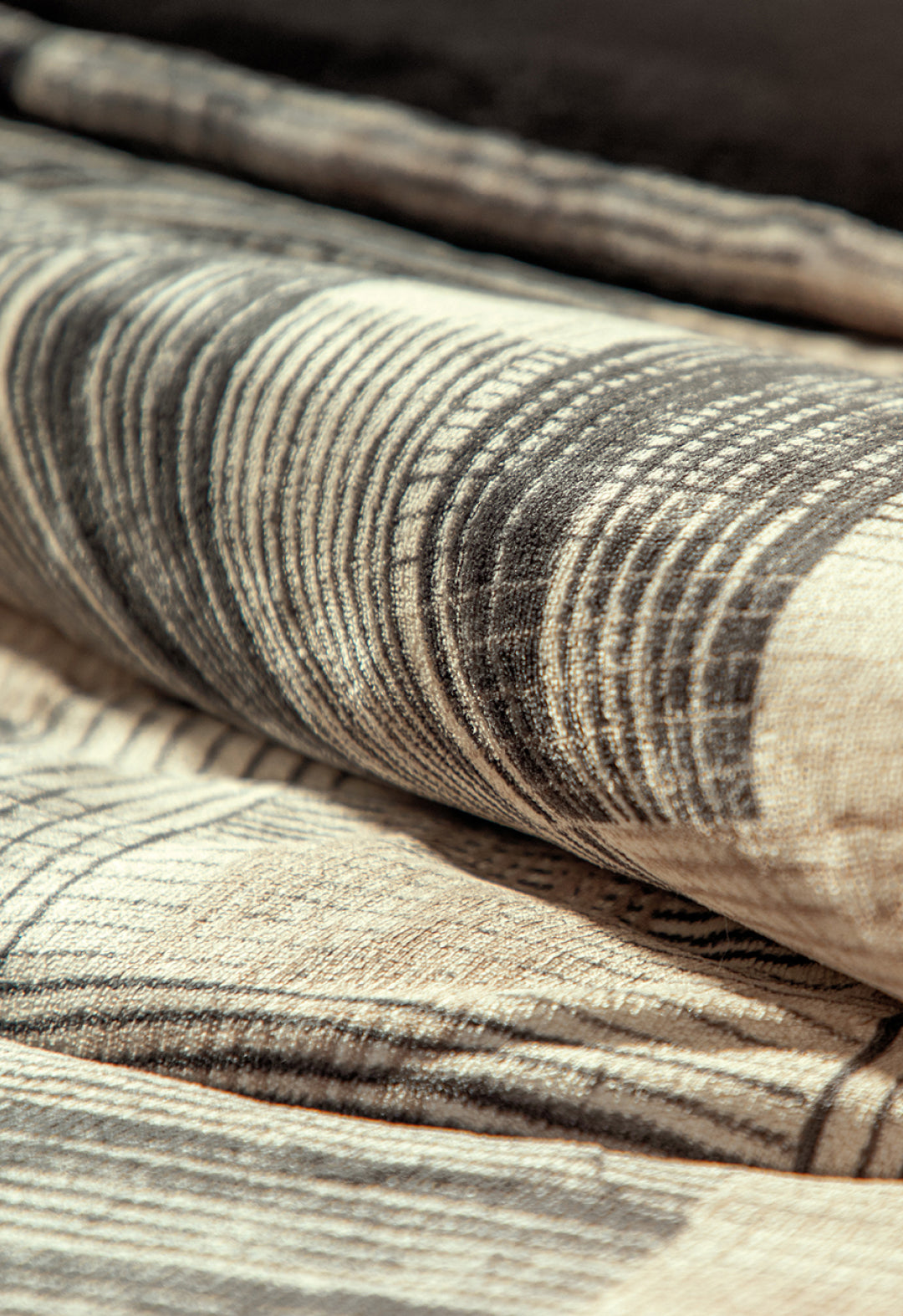 A close-up of folded fabric from the Coordinado de Cobertor Digital Soft Big Ben by Intima Hogar, showing textured circular and linear patterns in beige and dark brown—ideal for cobertores franela or fundas decorativas.