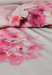Close-up of the Coordinado de Cobertor Digital Soft Florecer by Intima Hogar, showcasing a watercolor-style print of pink and white flowers with soft, blurred edges and delicate blossoms on a light background.