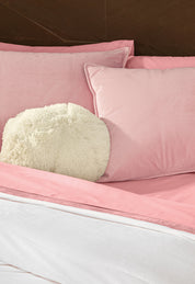 A neatly made bed with Intima Hogar's Coordinado de Cobertor Digital Soft Florecer, pink pillowcases and sheets, a fluffy round white pillow in front, all set against a dark wooden headboard.