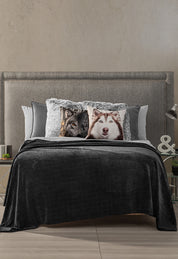 A modern bedroom features the Intima Hogar Coordinado de Cobertor Digital Soft Nebraska, a gray upholstered headboard, neat bedding, wolf and husky decorative pillows, plus side tables with lamps, small plants, and a decorative & sign.