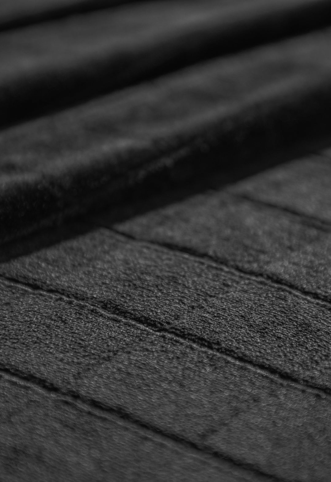 Close-up of a textured black surface with parallel, slightly raised lines—evoking the refined detail on the Coordinado de Cobertor Digital Soft Nebraska by Intima Hogar. Subtle shadows highlight the ridges, adding depth to the image.