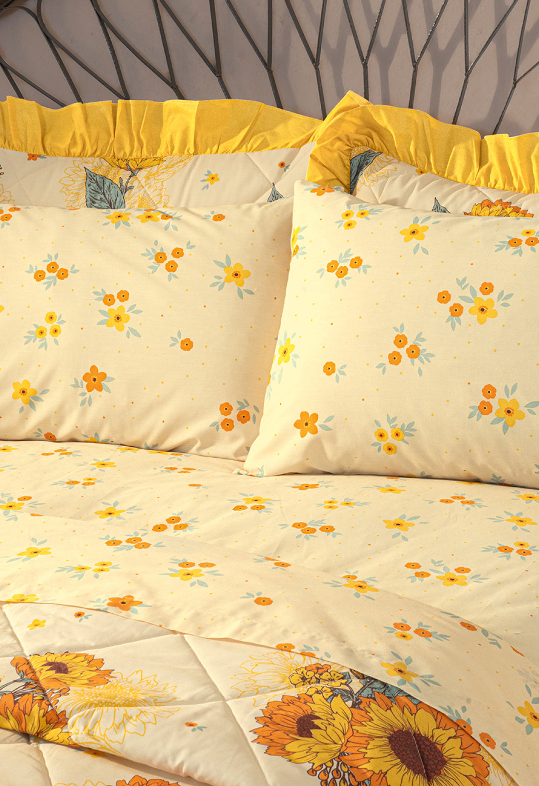 A neatly made bed features the Intima Hogar Coordinado de Colcha Doble Olán Girasoles with yellow and orange floral bedding, ruffled pillowcases, and a geometric headboard design.