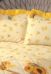 A neatly made bed features the Intima Hogar Coordinado de Colcha Doble Olán Girasoles with yellow and orange floral bedding, ruffled pillowcases, and a geometric headboard design.