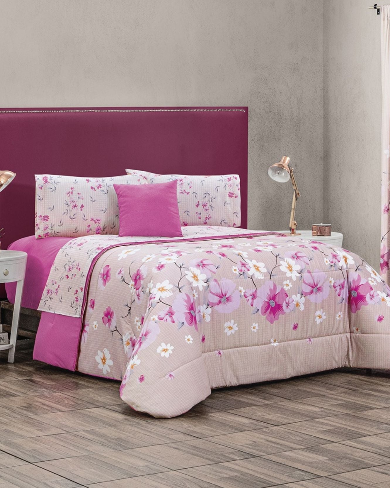 A neatly made bed with the Coordinado de Edredón Super Suave Anahí by Intima Hogar, matching pillows, and a magenta headboard. The room boasts wood floors, light walls, a white nightstand, and a gold lamp—ideal for a romantic look.