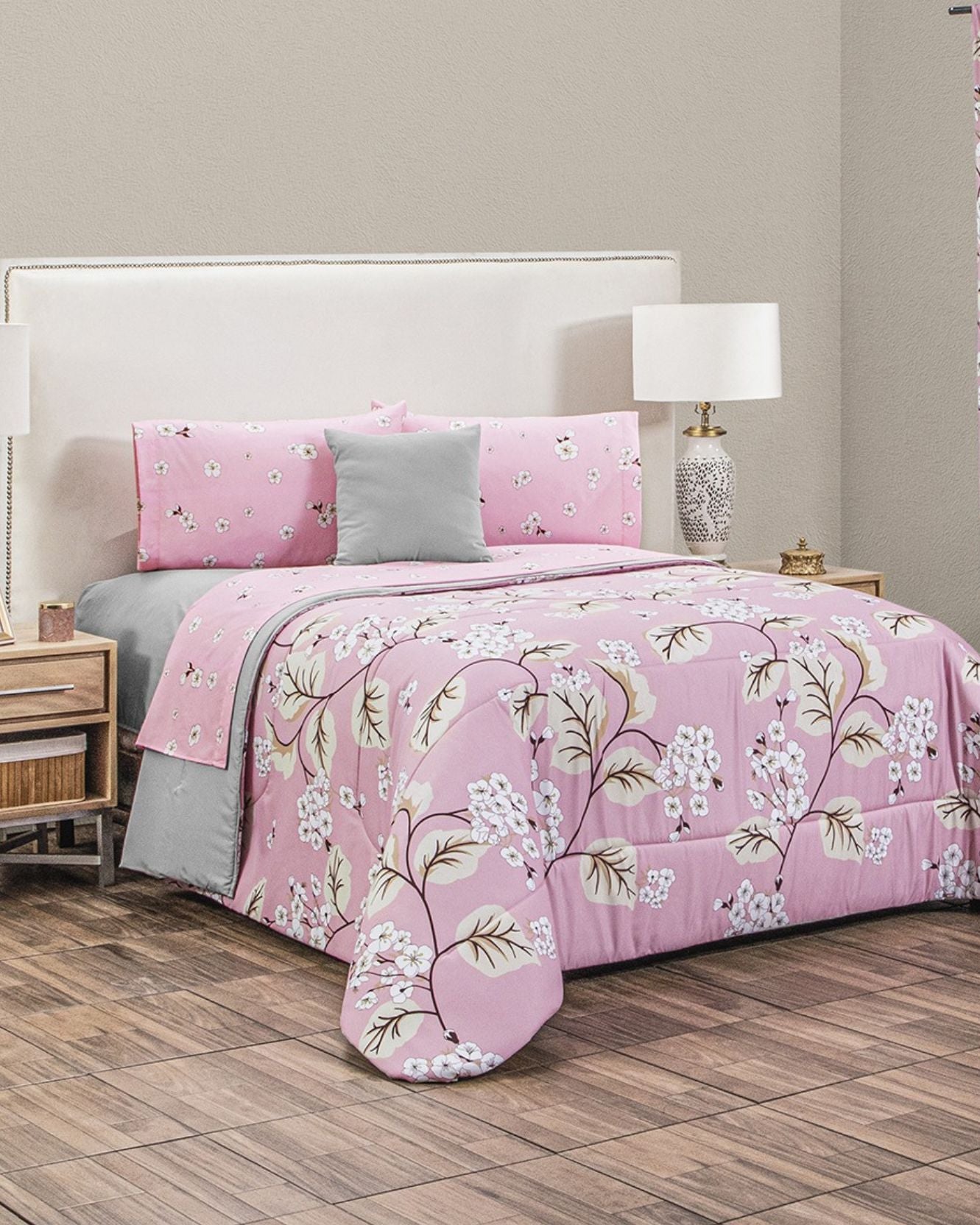 A neatly made bed with the Coordinado de Edredón Super Suave Katia by Intima Hogar adds encanto a la habitación romántica, with its pink floral design and matching pillowcases. Wooden nightstands and floors complete this inviting space.