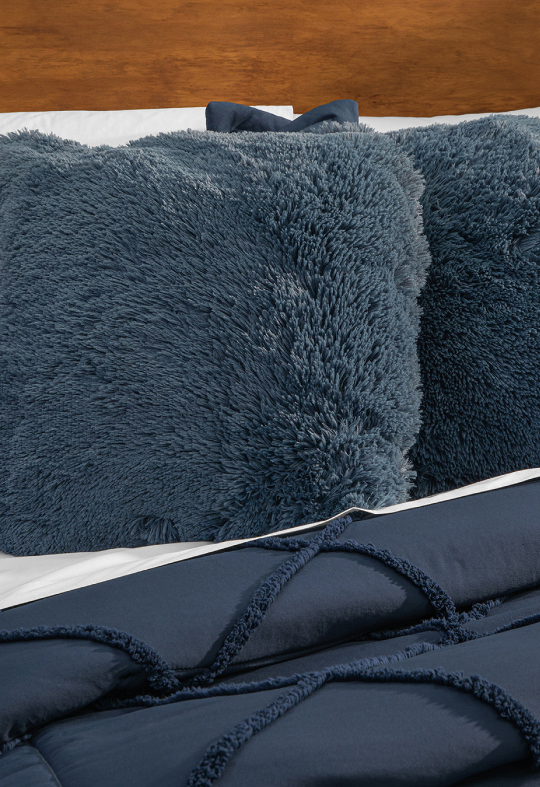 A close-up of a bed featuring fluffy, dark blue pillows and the Intima Hogar Coordinado de Edredón Luxury Seúl in navy, set against a wooden headboard.