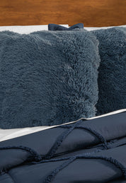 A close-up of a bed featuring fluffy, dark blue pillows and the Intima Hogar Coordinado de Edredón Luxury Seúl in navy, set against a wooden headboard.