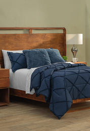 A wooden bed features the Coordinado de Edredón Luxury Seúl by Intima Hogar, paired with white Royal Cotton sheets and pillows. A bedside table holds a lamp, cup, and small plant in a light-walled room with wood floors.