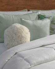 The Funda de Almohada Ensueño Verde Pistacho de Intima Hogar decora la cama, combinando con edredón blanco y cojines verdes, creando un espacio acogedor junto al cabecero de madera.